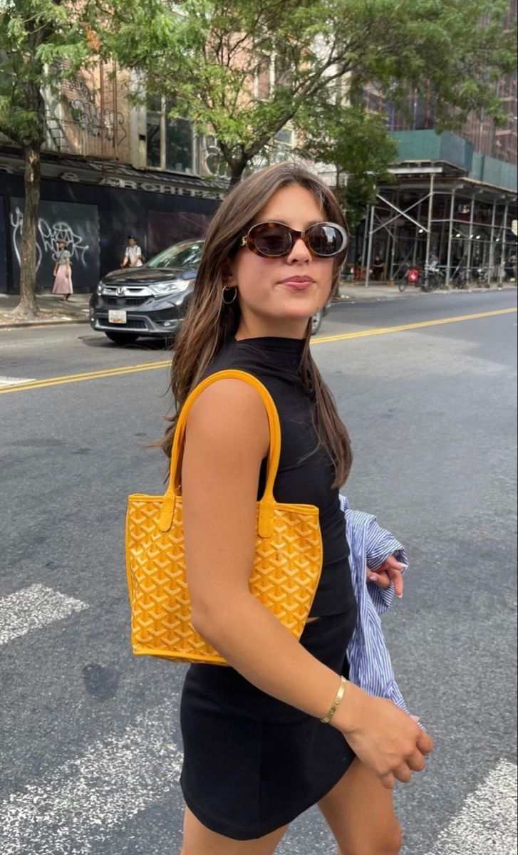 Woman wearing sunglasses carrying a yellow geometric patterned mini tote bag on city street